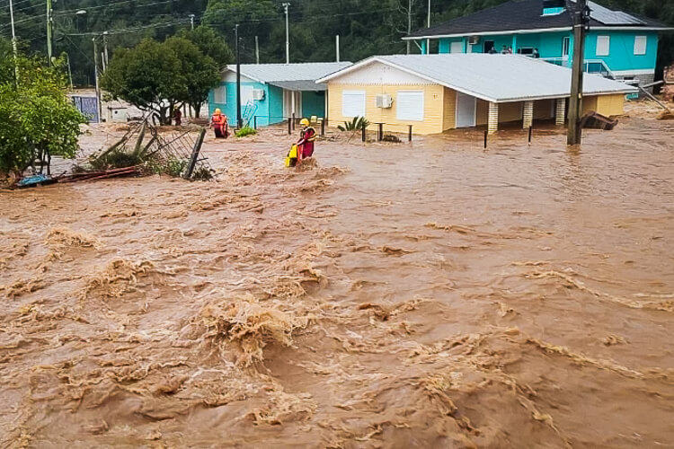 Uma rua com enchente, após chuvas intensas. Bombeiros no meio da água para proteger as pessoas