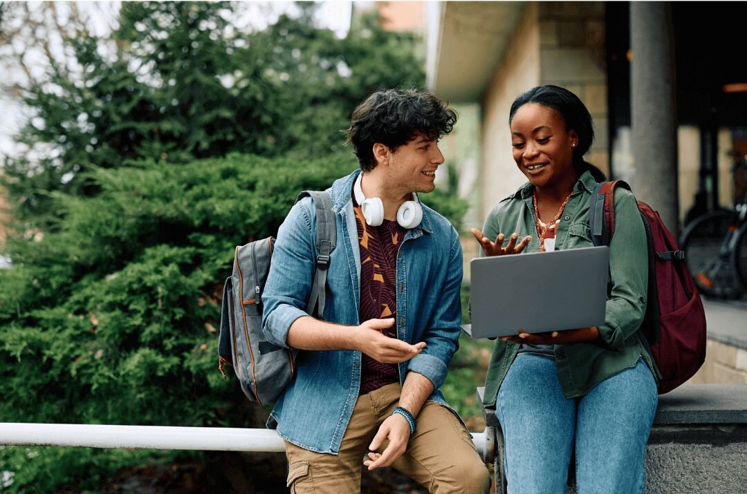 Um aluno conversando com uma aluna que tem um notebook na mão.